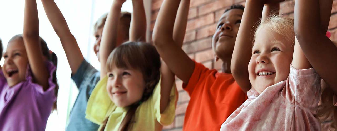 A group of childen standing together holding hands raised in the air.