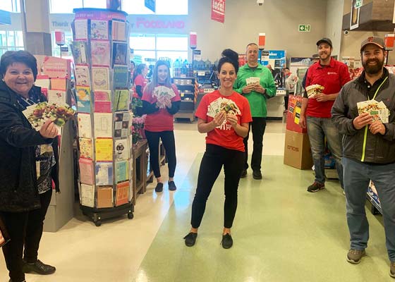 A group of Foodland employees and customers holding gift cards while physical distancing.