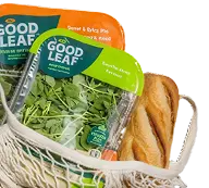 Packaged GoodLeaf greens and a loaf of bread in a string tote bag.
