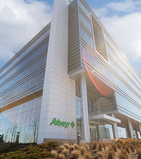 Sobeys corporate office building with glass exterior and landscaped entrance in daylight.